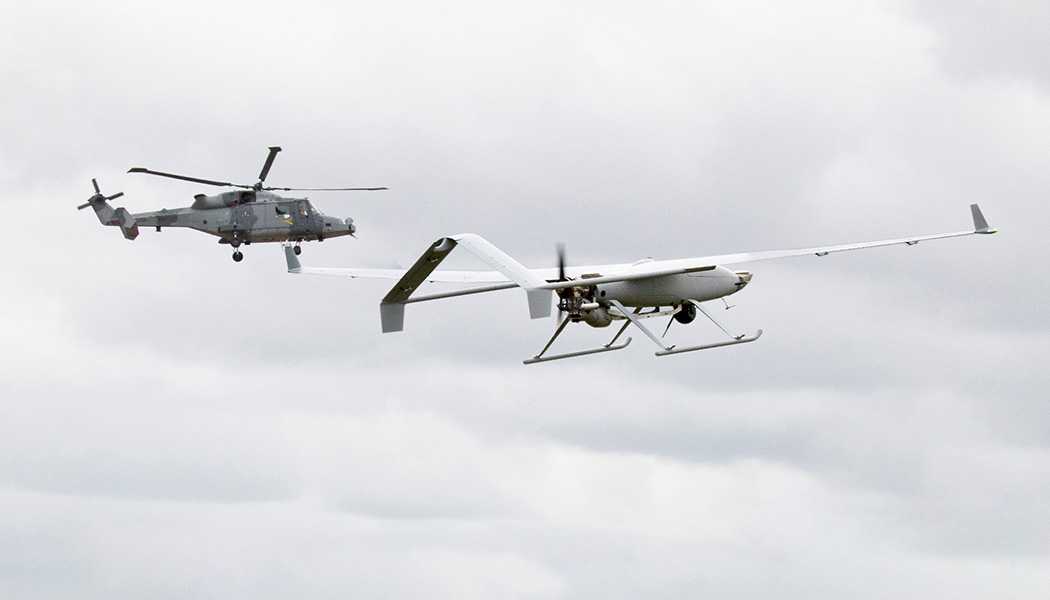 A drone in flight with a helicopter in the background